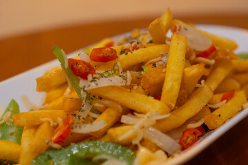 spicy french fries with chilli, garlic, bell pepper, and anchovy toppings, served on white long plate on wooden table surface