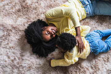 A mother and child are laying on a carpet, the child is wearing a yellow sweater - Powered by Adobe