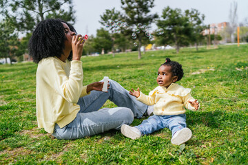 A woman and a child are sitting on the grass, blowing bubbles