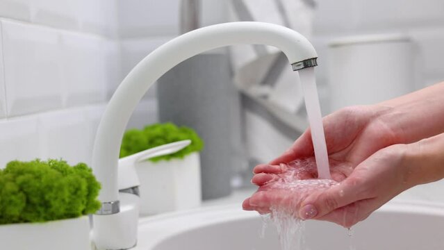 A girl draws clean water into her hands from a tap in the kitchen in a bright interior