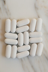arranged grid of white pills, vitamins on white marble background