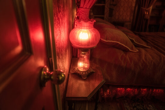 This image shows an antique bedside lamp illuminating a curated victorian bedroom in red light.