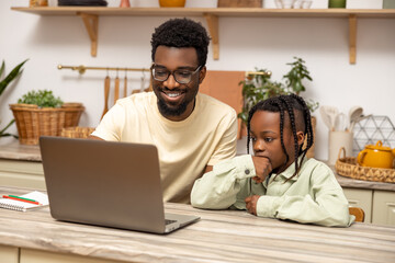 Black man with his daughter using laptop together while doing homework