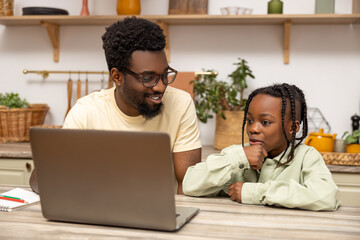 Black man with his daughter using laptop together while doing homework