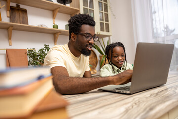 Black man with his daughter using laptop together while doing homework