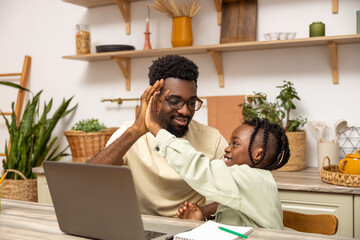 Black father with daughter doing online tasks on laptop