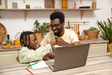 Black father with daughter doing online tasks on laptop
