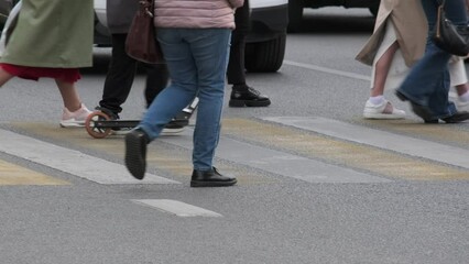 A group of people crosses the road at a pedestrian crossing on the street during the day. Frame of legs unrecognizable