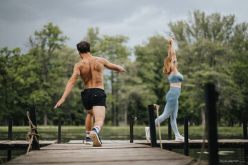 A couple is exercising on a wooden dock by a lake, surrounded by green trees and cloudy sky,...