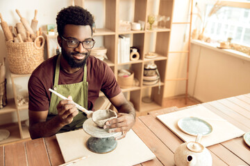 Smiling man painting pottery and looking enjoyed