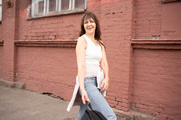 a woman in jeans with a backpack walks cheerfully and quickly down the street. walk in summer, spring in good weather