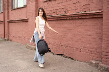 a woman in jeans with a backpack walks cheerfully and quickly down the street. walk in summer, spring in good weather