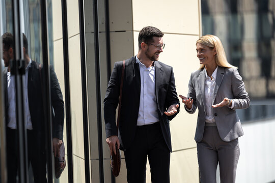 Smiling man and woman colleagues walking outdoor discussing business ideas