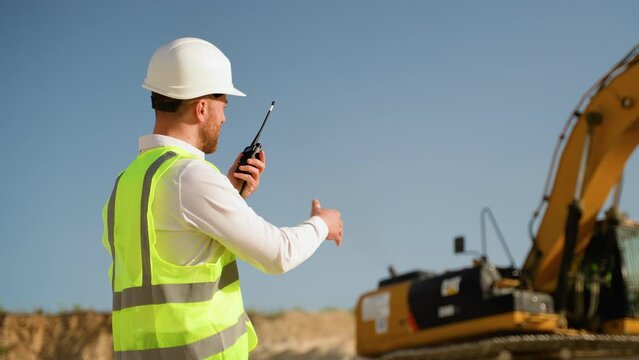 Foreman giving commands to employee in excavator using walkie talkie at construction site