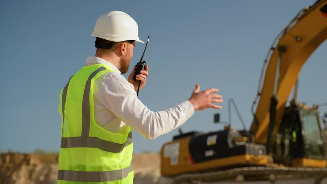 Foreman giving commands to employee in excavator using walkie talkie at construction site