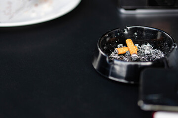Black ashtray with cigarette butts and ashes