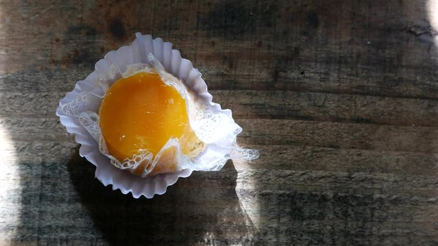 A very slow zoom in on an egg custard on the table (Quindim candy). Rays of sunlight randomly moving over an egg dessert. Close-up of an egg yolk custard. A Brazilian coconut custard under sunbeams.