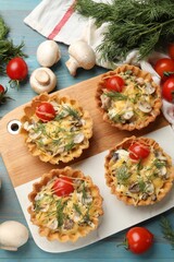 Tasty tartlets with cheese, tomatoes, mushrooms and dill on turquoise wooden table, flat lay