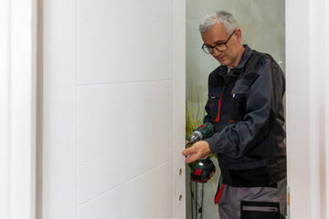 Installation of a lock on the wooden door. Screwdriver is used by carpenter to install lock handles in room door