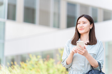 オフィスビルの前でスマホを操作する若いアジア人ビジネスウーマン
