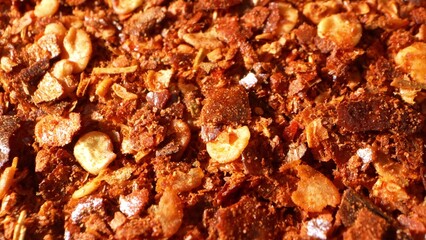 A close-up of ground chili reveals its coarse texture, brimming with visible seeds and flakes. The striking reddish-brown hue signifies the bold spiciness and robust flavor inherent to chili peppers.
