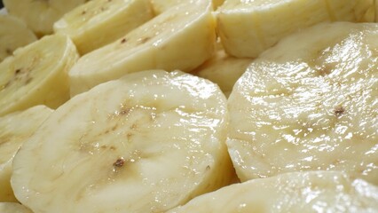 Zoom in on nature's canvas, behold the symphony of sliced bananas-creamy, delicate, with a golden hue, adorned by quaint brown freckles, inviting a tantalizing dance with every slice.
