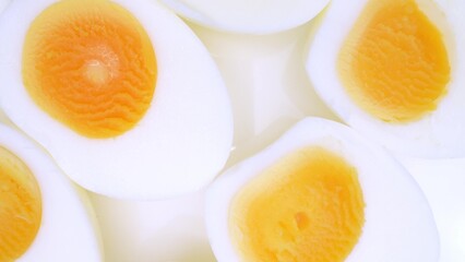 In this close-up, halved boiled eggs showcase vibrant yellow yolks nestled within pristine, smooth...