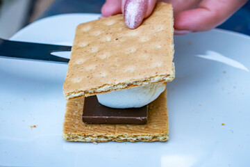 The making of a smore:  A graham cracker is placed on top of a roasted marshmallow.