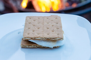 The making of a smore:   Finished smore ready to eat.  Campfire in background.