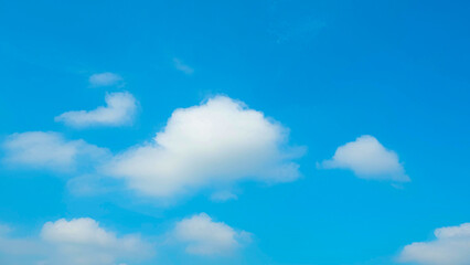 A bright blue sky filled with a few scattered, fluffy white clouds. The contrast between the vibrant blue and the soft white creates a peaceful and calm atmosphere. Blue sky background.
