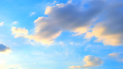 A bright blue sky adorned with scattered clouds. The clouds appear fluffy and are illuminated with...