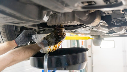 A mechanic drains a car's used engine oil.