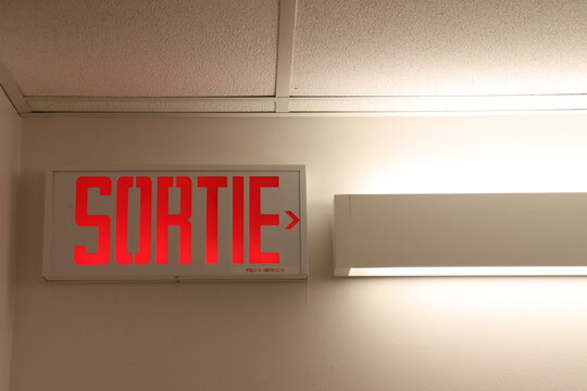 A sign on a wall with the word ''sortie''. Interior sign in red color and for the exit direction in french.
