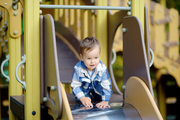 Cute baby boy having fun on outdoor playground. Active sport leisure for toddlers. Child on slide