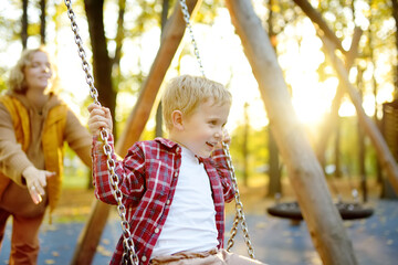 A mother swings her son on a swing in an autumn city park. A beautiful woman entertains her adorable baby on the playground.