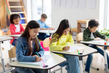 Engaged pupils children sitting at desks, writing in copybooks, having test, creating studious...