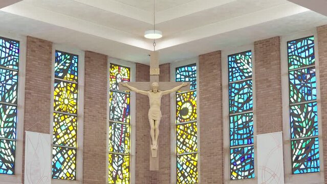 Jesus hanging on a crucifix or cross in front of stained glass windows in a catholic cathedral church during mass.