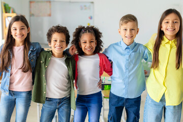 Group portrait of happy diverse school friends. embracing and posing in classroom, looking at the camera and smiling