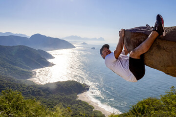 Adventurous climber hangs off Pedra do Telégrafo with breathtaking coastal view in Rio de Janeiro