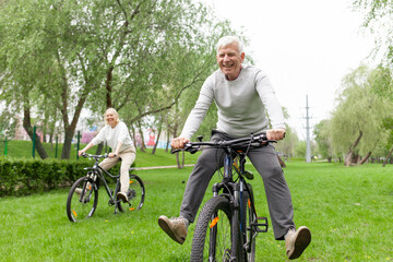 elderly senior couple rides bicycle in the park in the summer and smiles, old gray-haired man and woman are actively resting outdoors, old people practice cycling in forest