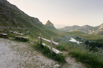 Wooden bench overlooking a majestic mountain vista invites peaceful contemplation. The setting sun casts a warm glow over the rugged landscape, promising adventure