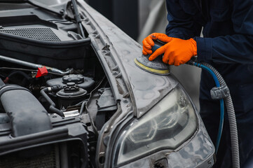 A mechanic sands the putty on a car body with a machine. Repair after an accident. 