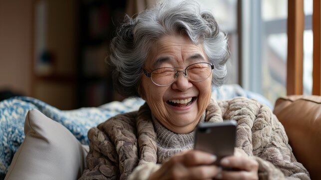 Senior Asian woman laughing while using smartphone at home.