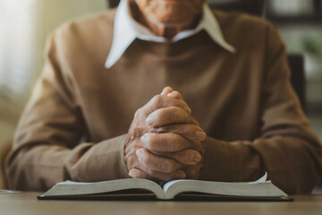 Old man's hands folded in prayer on a Holy Bible in church concept for faith, spirituality, and...