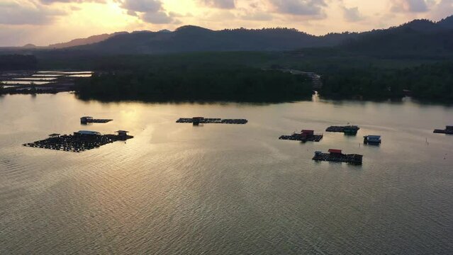 A traditional offshore floating fish farm on calm waters, aquaculture facility to raises fish and shrimps, sunset aerial view.