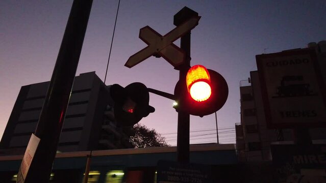 Red lights blinking, sunset night train passing by background skyline downtown