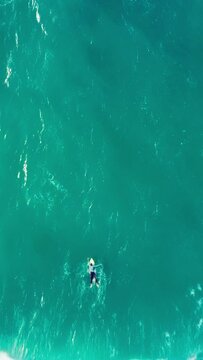Vertical Screen: A serene scene of a person paddling on a surfboard in clear turquoise waters, capturing a peaceful moment in a beautiful ocean setting, invoking tranquility and relaxation