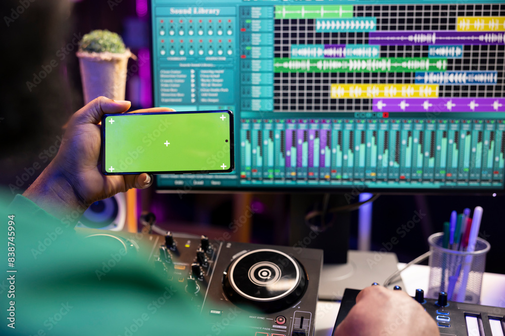 Poster Music producer operating on daw software in home studio and using an isolated display on smartphone, working on new songs. Professional technician adjusting volume levels with mixing console.