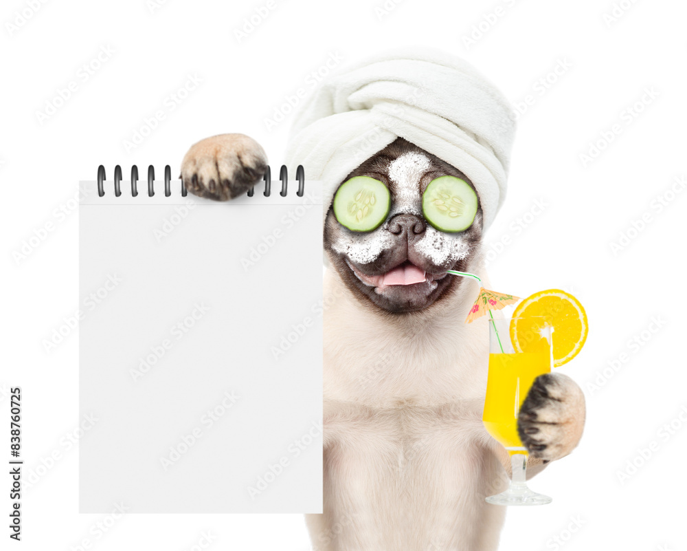Fototapete Funny Mastiff puppy with towel on it head and with pieces of cucumber on it eyes holds orange cocktail and shows empty list. Top down view