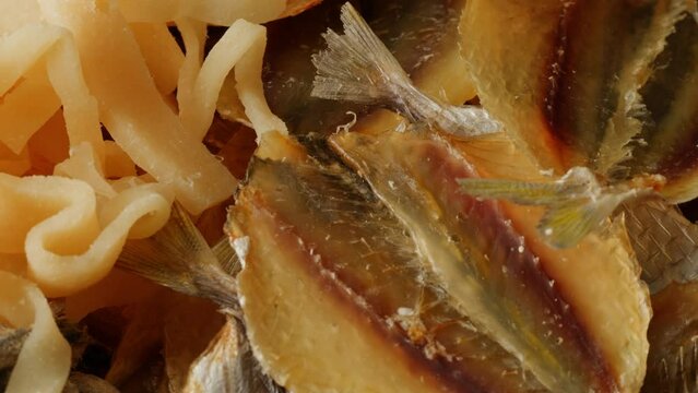 Dry mix of fish snack on wooden plate close-up. Salted squid rings, anchovies, pollock, cod fish snacks for friends company and beer. 